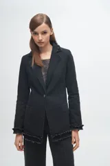 Blazer de denim azul con solapas y puños decorados con volados desflecados. Presenta un corte estructurado con bolsillos laterales y cierre frontal.