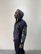 Campera reversible con cierre frontal. Un lado confeccionado en algodón azul marino con estampa plastisol, bordados con apliques y capucha. El otro lado presenta un diseño de polar de pelo largo en color gris. Posee corte oversize, puños y ruedo acanalados.