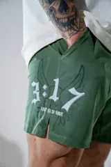 Short deportivo de color verde militar, con diseño estampado en blanco que incluye números y alas. Presenta aberturas laterales en el ruedo para mayor movilidad y bolsillos laterales.