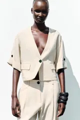 Chaqueta corta de escote en pico con cierre frontal de un botón. Presenta mangas cortas con detalle de vuelta, trabilla y botón, además de falsos bolsillos delanteros con solapa.