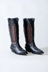 Bota texana de cuero negro con apliques de cuero marrón en los laterales y pespuntes en color crema. De caña media/alta y taco bajo. Diseño calado con motivos geométricos.