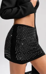Conjunto de dos piezas compuesto por un blazer corto tipo torera de manga larga y una minifalda ajustada con detalle de strass brillante. La falda presenta un diseño drapeado y la chaqueta tiene un corte estructurado.
