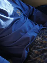 Pijama de dos piezas compuesto por una camiseta de manga larga azul marino con logo bordado en el pecho y un pantalón largo de corte recto con estampado de cuadros en tonos azul y verde.