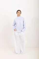 Camisa de manga larga a rayas celestes y blancas, con cuello alto mao y volados frontales a lo largo de la botonadura.