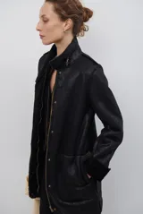 Chaquetón de efecto cuero en color marrón, con interior y detalles en corderito color bordó. Presenta cierre frontal con cremallera y botones a presión, cuello solapa y mangas largas con puños de corderito.