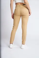 Pantalón de gabardina corte skinny, color beige, con diseño de cinco bolsillos, cierre de cremallera y botón frontal.