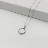 Conjunto de cadena y dije plateados. El dije es una medalla redonda con borde de pequeñas circonias y centro liso.