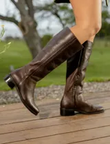 Bota de cuero vacuno color marrón, con caña alta, suela de goma y cierre lateral.