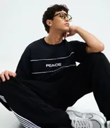 Remera oversized negra de algodón con cuello redondo, mangas cortas amplias y estampado frontal con la palabra "PEACE" en blanco, acompañada de dos líneas horizontales blancas.