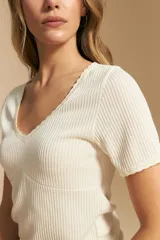 Remera de manga corta en tejido acanalado, con escote en V y detalles de puntilla en el borde del escote y en las mangas. Presenta un ajuste entallado al cuerpo.