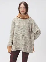 Sweater polerón de tejido de punto jacquard color beige con textura melange, cuello alto y puños acanalados en tono tostado con detalles de pespuntes negros. Presenta corte holgado y aberturas laterales en el dobladillo.