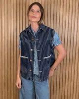 Chaleco de denim azul oscuro con diseño a rayas verticales, cuello camisero, cierre frontal con botones y bolsillos frontales con detalles de costuras bordadas en color blanco en los bordes y sisas.