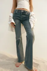 Jean de denim azul medio con leve efecto desgastado, corte ajustado hasta la rodilla y pierna acampanada (bootcut). Modelo de tiro bajo con cierre y botón, bolsillos abiertos delanteros y bolsillos traseros con solapa y botón.