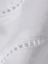 Vestido camisero corto color blanco, confeccionado en algodón orgánico. Presenta cuello en V, cierre frontal con botones, mangas largas abullonadas, cinturón de lazo ajustable en la cintura, bolsillos laterales y detalle de encaje calado en forma de escalera.