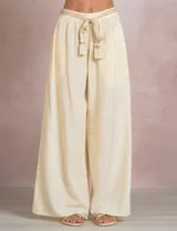 Pantalón palazzo de tiro alto marca Elan, en color beige, confeccionado en mezcla de algodón, viscosa y lino. Presenta cintura delantera plana con parte trasera elastizada, bolsillos laterales funcionales y corte de pierna ancha. Incluye un cinturón trenzado al tono con terminación en borlas y flecos.