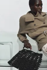 Bolso tipo shopper pequeño de crochet negro, con asas de hombro de material liso negro y una bolsa interior con cierre de cremallera.