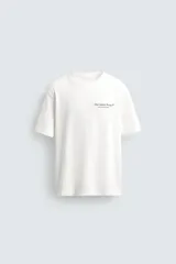 Camiseta de corte relajado, color blanco, con cuello redondo y manga corta. Presenta un pequeño estampado en el pecho con texto y un diseño gráfico más grande en la espalda.