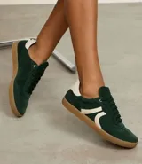 Championes de mujer estilo chuteira, color verde oscuro con detalles en blanco y suela de goma color caramelo. Presentan un diseño de corte bajo con cordones y un logo lateral en forma de arco.