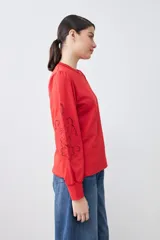 Sweatshirt de algodón color rojo, con cuello redondo y mangas largas abullonadas que presentan detalles de calados bordados. Posee puños elásticos y un diseño holgado.