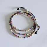 Cuerdita para lentes de tela tejida con patrón multicolor, con terminales metálicos plateados y sujetadores de goma negra en los extremos.