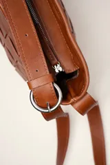 Cartera tipo morral de cuero color beige, con diseño trenzado artesanal, correa larga regulable y cierre superior.