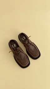 Zuecos de punta cuadrada color marrón, confeccionados en cuero, con cordones de cuero en la parte superior.