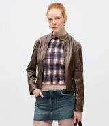 Campera biker de cuello alto confeccionada en poliuretano con efecto marmorizado. Presenta cierre frontal, bolsillos laterales con cremallera, recortes estructurados y detalles de botones a presión en el cuello y laterales.