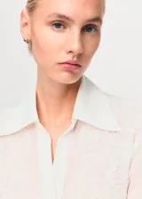 Camisa de corte recto y diseño clásico con cuello camisero, manga larga con puños abotonados y cierre frontal de botones ocultos. Presenta parches decorativos sutiles en la parte frontal.