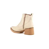 Bota de caña baja realizada en cuero engrasado color beige, con punta redondeada y cierre lateral. Presenta un taco cuadrado de madera de 5 cm de altura y suela con plataforma.