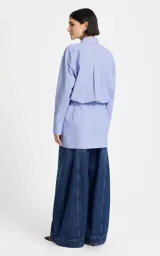 Vestido camisero corto de algodón en color celeste con finas rayas blancas, con diseño asimétrico tipo wrap, mangas largas y escote en V con cuello camisero.