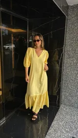 Vestido largo color amarillo pálido, con escote en V, mangas cortas abullonadas con detalle de calado y ruedo con volantes y calado.