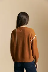 Sweater de punto color marrón con diseño de líneas blancas en contraste. Presenta cuello redondo, mangas largas y puños tejidos, con una estética minimalista y moderna.