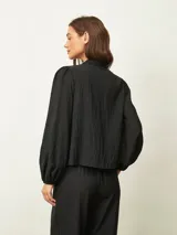 Blusa de textura arrugada con cuello alto y lazo frontal para anudar. Presenta mangas largas con puños elásticos y corte recto.