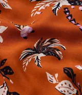 Vestido corto color ladrillo con estampado de flores y palmeras en tonos blanco y negro. Tiene escote cuadrado, mangas cortas abullonadas y falda con volantes.