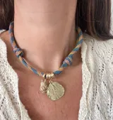 Gargantilla con cordón doble en tonos naranja y gris, con dije de concha dorada y dije de caracol blanco.