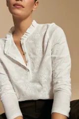 Blusa de algodón color azul con textura bordada, cuello con volado y cierre frontal con botones. Presenta mangas largas y un calce relajado.