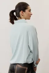 Buzo celeste de manga larga con cuello polo y cierre frontal de botones. Presenta un parche marrón bordado en el pecho.