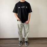 Remera oversize blanca de manga corta con detalles de líneas negras en las costuras de los hombros y mangas. Presenta un gran estampado en la espalda con el número 99 en diseño rayado y el logo de la marca en la parte superior.