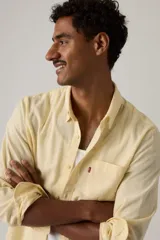Camisa de manga larga color amarillo claro, con cuello camisero, cierre frontal de botones y un bolsillo aplicado en el pecho con etiqueta roja de la marca.