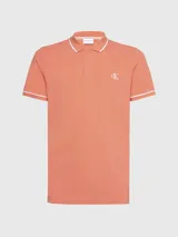 Chomba color salmón de corte slim fit, con cuello clásico y tapeta de dos botones. Presenta ribetes blancos en cuello y mangas, y logo CK bordado en blanco en el pecho.
