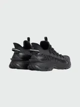 Championes Moncler modelo Trailgrip Lite2 de color negro, diseñados para trekking y actividades al aire libre. Presentan una silueta robusta, suela dentada Vibram, cordones redondos gruesos, tiradores en la lengüeta y el talón, y el nombre de la marca grabado en el lateral.