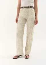 Pantalón de jean tiro medio, color crema o blanco roto, con estampado sutil en tono grisáceo. Corte recto o ligeramente acampanado.