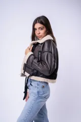 Campera tipo gamulán de cuero sintético marrón oscuro con interior y detalles de corderito sintético en cuello y puños. Presenta cierre frontal, bolsillos laterales con cierre y correas ajustables en el cuello.