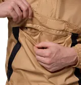 Chaqueta tipo cortaviento Columbia con diseño de media cremallera y capucha ajustable. Presenta un bolsillo frontal grande con solapa y un bolsillo adicional con cierre en la manga. Combina tonos beige y negro, con tecnología Omni-Shield que repele la humedad y las manchas.