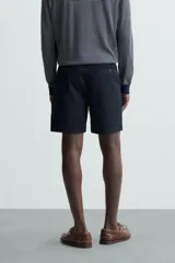 Bermuda de hombre color beige claro, corte regular fit, con pliegues frontales, bolsillos delanteros y bolsillos traseros de doble vivo con botón.