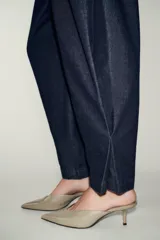 Pantalón de denim azul oscuro, tiro alto, con pinzas delanteras que generan volumen en la cadera y pernera ancha y recta. Presenta cierre frontal y bolsillos laterales.
