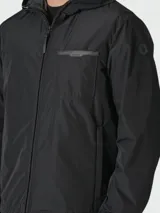 Chaqueta ligera con capucha, color negro, con cierre frontal de cremallera, bolsillo en el pecho y puños elásticos.