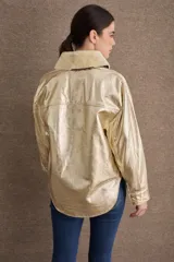 Campera de cuero metalizado color dorado con cuello de corderito sintético en tono crema. Presenta cierre frontal con botones metálicos, bolsillos frontales con solapa y diseño de corte recto.