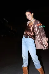 Pantalón de jean celeste claro, corte boyfriend, con laminado dorado en la parte inferior de la pierna y cinturón de cuero marrón.