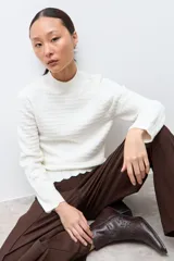 Sweater de punto color crudo con cuello alto tipo media polera, manga larga y diseño con textura de líneas horizontales. Presenta un borde inferior con terminación ondulada.